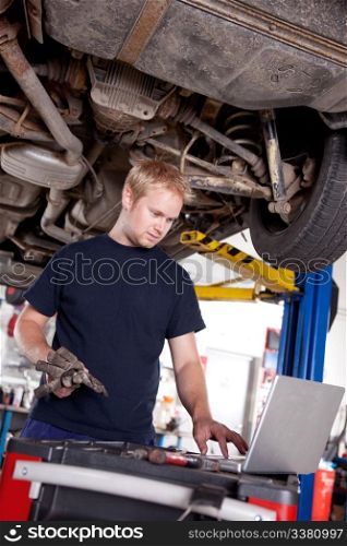 A mechanic in a garage looking at a laptop