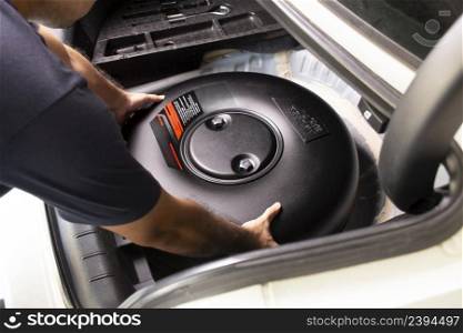 A mechanic is installing a car donut-shaped LPG tank in a spare wheel hole in a auto repair garage