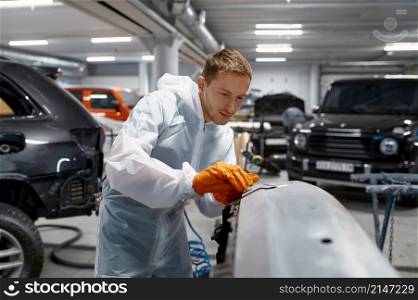 A mechanic puttying car body. Local repair after accident before painting in service workshop. Mechanic engaged in local repairing car body