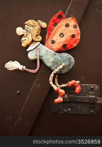 A mechanical caricature that is carved from wood adorns a door in Prague. This fairy godmother with ladybug has legs and wings which move as the door moves.