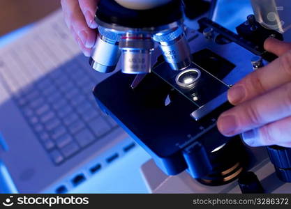 A medical or scientific researcher using a microscope and laptop