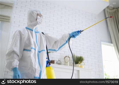 A medical staff in PPE suit is using disinfectant spray in living room, Covid-19 protection , disinfection concept .. A medical staff in PPE suit is using disinfectant spray in living room, Covid-19 protection , disinfection concept