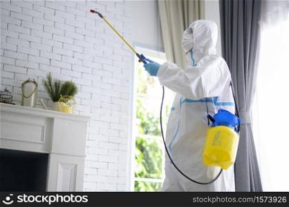 A medical staff in PPE suit is using disinfectant spray in living room, Covid-19 protection , disinfection concept .. A medical staff in PPE suit is using disinfectant spray in living room, Covid-19 protection , disinfection concept