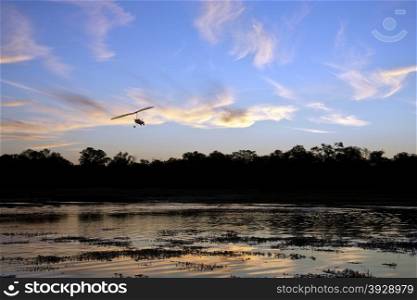 A microlight aircraft flying over a channel in the Okavango Delta in Botswana at sunset