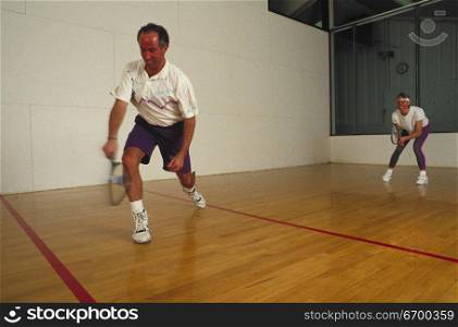 A mid adult man and woman playing indoor squash