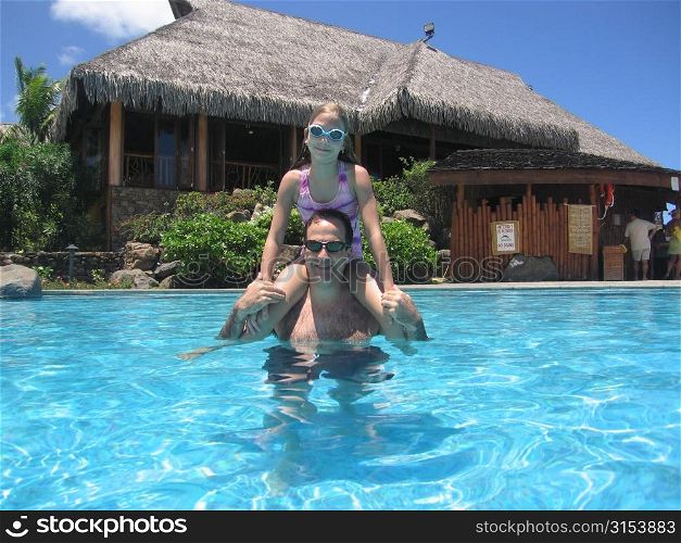 A mid adult man carrying his young daughter (12-13) on his shoulders in water Moorea, Tahiti, French Polynesia, South Pacific