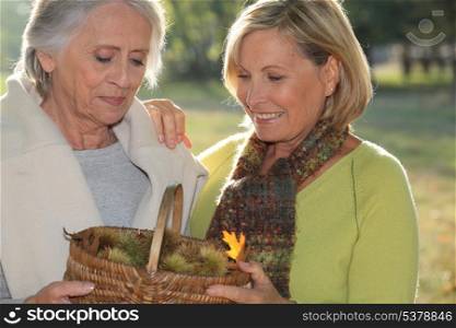 a mid age blonde woman and an older woman holding a wickerwork basket full of chestnuts