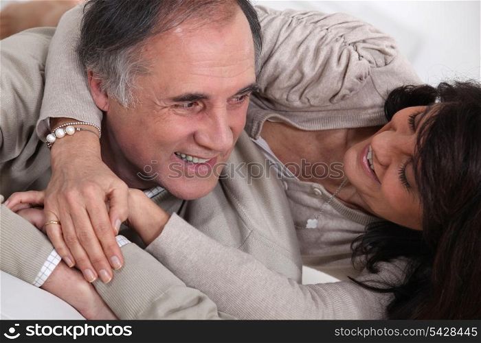 A middle age couple fooling around in bed.
