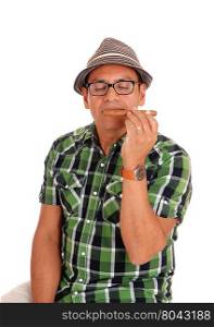 A middle age Hispanic man enjoying the smell of his big cigar, sitting and wearing a beige hat, isolated for white background.