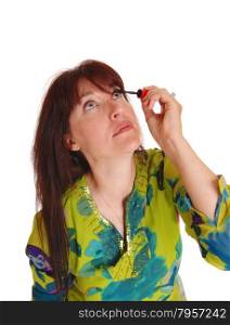 A middle age woman in a colorful dress looking up and putting makeupon her eyelashes, isolated for white background.