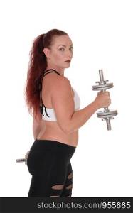 A middle age woman standing in profile lifting her two dumbbells whit her long red hair and workout outfit, isolated for white background
