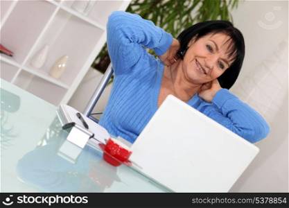 A middle age woman stretching in front of her computer.