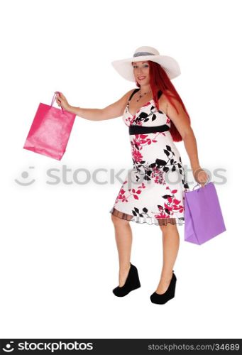 A middle age woman, wearing a white hat and holding some shoppingbags, standing isolated for white background.