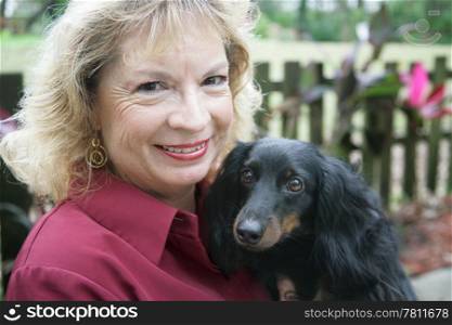 A middle aged blond woman and her long haired daschund in the park. Focus on the woman&rsquo;s face.