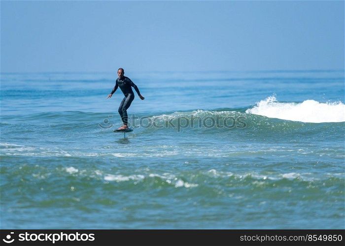 A middle aged man doing some foil surfing or hydrofoil surfing in the sea on a bright sunny day.