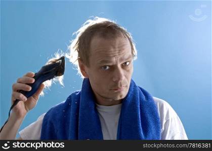 A middle aged man dressed in a white t-shirt, shaving his own hair with a clipper