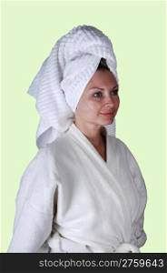 A middle aged woman in a white bathrobe and a towel around her hairstanding in the studio looking into the camera.