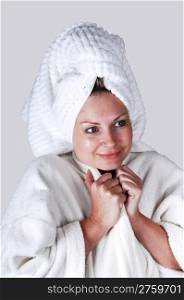 A middle aged woman in a white bathrobe and a towel around her hairstanding in the studio looking into the camera.