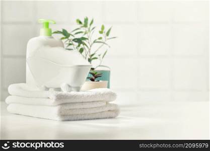 A miniature bubble bath, shampoo, flowers and white towels on bathroom countertop, copy space