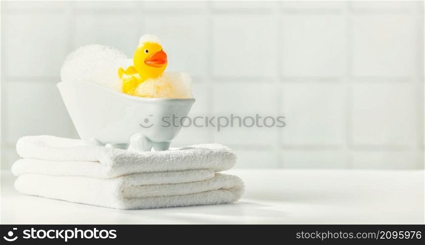 A miniature bubble bath, yellow rubber duck and white towels on bathroom countertop, children bath accessories, baby care, space for text