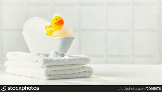 A miniature bubble bath, yellow rubber duck and white towels on bathroom countertop, children bath accessories, baby care, space for text