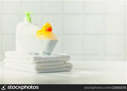 A miniature bubble bath, yellow rubber duck and white towels on bathroom countertop, children bath accessories, baby care, copy space
