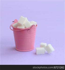 A miniature pink bucket filled with cubes of sugar lies on a purple pastel background. Minimal concept.. A miniature pink bucket filled with cubes of sugar lies on a purple pastel background. Minimal concept