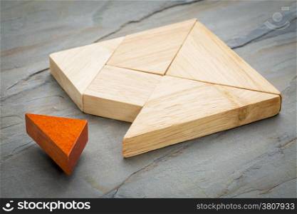 a missing piece in a square built from tangram shapes, a traditional Chinese puzzle game, slate rock background