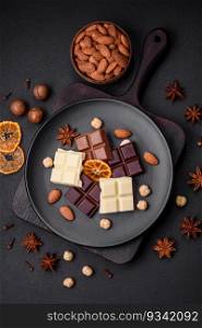 A mix of several types of delicious sweet chocolate broken into cubes on a black plate on a dark concrete background