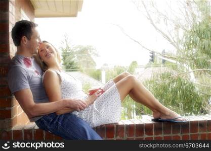 A modern 30&acute;s couple sin on balcony and conversing, Showing affection. Melbourne Australia.