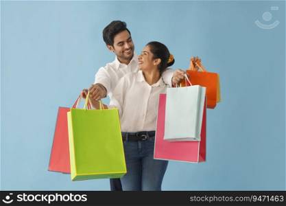 A MODERN COUPLE LOVINGLY LOOKING AT EACH OTHER WHILE HOLDING SHOPPING BAGS