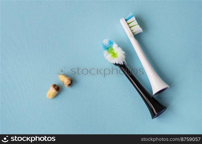 A modern electric toothbrush on a blue background next to extracted wisdom teeth affected by caries. Tooth extraction operation. Hygiene concept for daily care. Old and new toothbrush. A modern electric toothbrush on a blue background next to extracted wisdom teeth affected by caries. Tooth extraction operation. Hygiene concept for daily care. Old and new toothbrush.