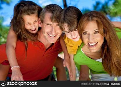 A modern family of father, mother, daughter and son playing together and having doing piggy back in a park