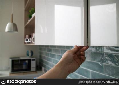 A modern kitchen design with a cabinet without handles, the hand of a man shows how doors open without handles with a special indent for hands on the background of blue tiles and kitchen interior. kitchen cabinet with doors without handles, the man&rsquo;s hand shows how the doors open without handles