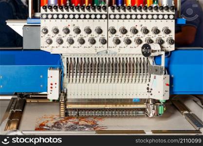 A modern programmable professional embroidery machine for embroidery on various fabrics creates patterns with multicolored spools of thread. Closeup. Copy space.. Industrial programmable embroidery machine with multicolored threads at work. Closeup. Copy space.