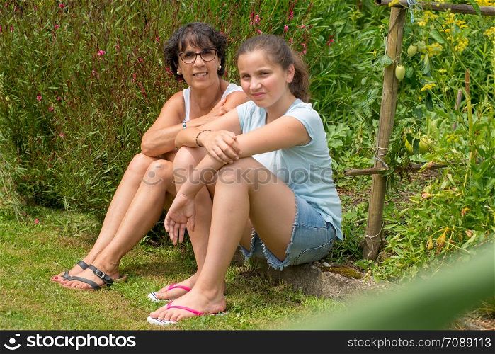 a mom and her teen daughter sit in the grass