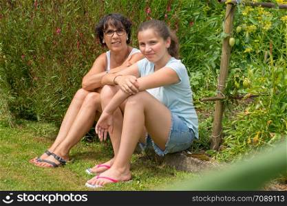 a mom and her teen daughter sit in the grass
