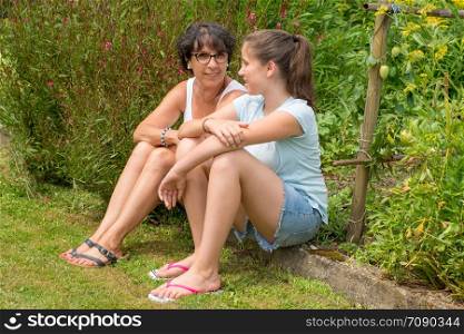 a mom and her teen daughter sitting in the grass