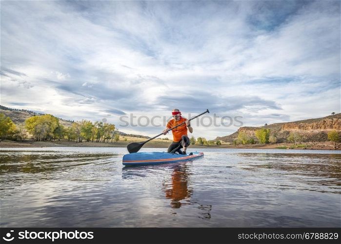 A moment of contemplation - a senior male on stand up paddleboard on a calm mountain lake