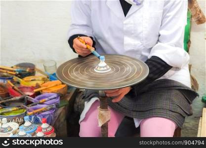 A Moroccan woman painting ceramic souvenir on the rotating table. Medina of Fez, Morocco.