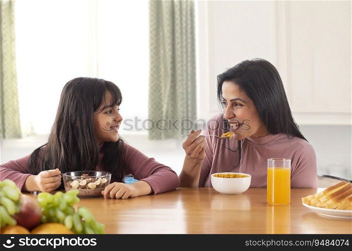 A MOTHER AND DAUGHTER HAPPILY EATING BREAKFAST TOGETHER