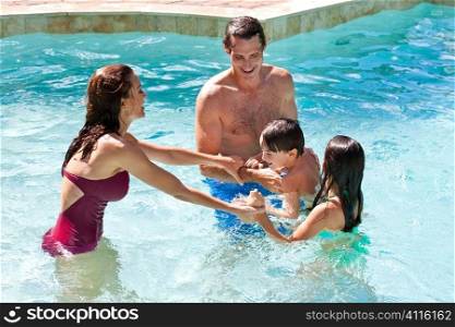 A mother and father having fun on vacation playing with their children on their shoulders in a swimming pool