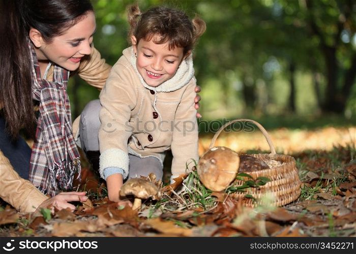 a mother and her little girl picking mushrooms in the forest