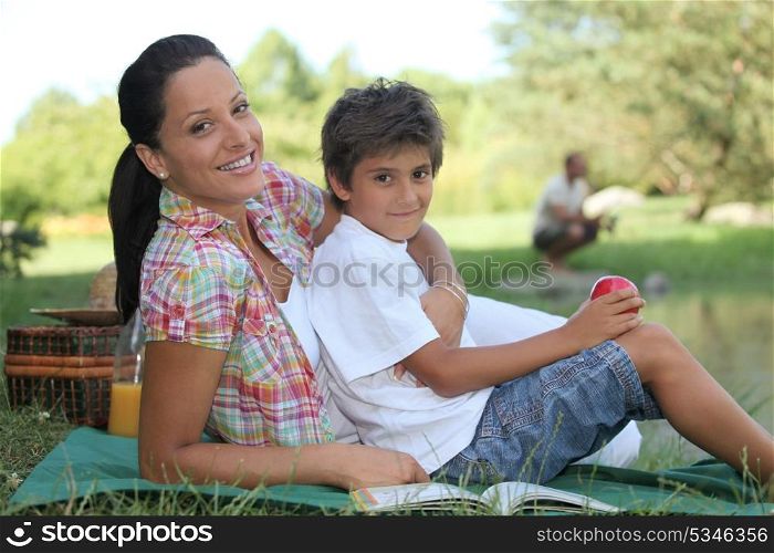 a mother and her son at picnic, the father is fishing