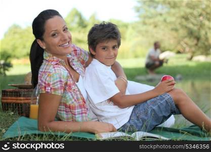 a mother and her son at picnic, the father is fishing