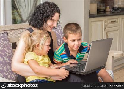 A mother and her two children, a girl and a boy, are looking with much interest at something on a silver laptop while sitting outside on the patio.