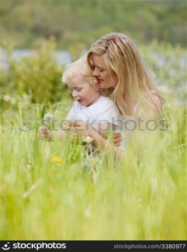 A mother and son making a wish on a dandelion in a green meadow