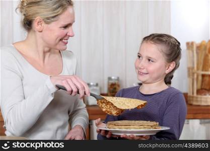 A mother cooking crepes with her daughter.