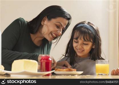 A MOTHER HAPPILY SPREADING JAM ON BREAD FOR DAUGHTER