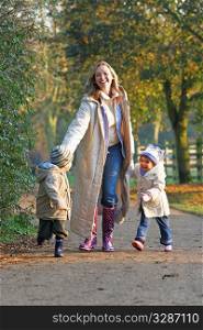 A mother, her son and daughter walking through a park filled with autumnal colors
